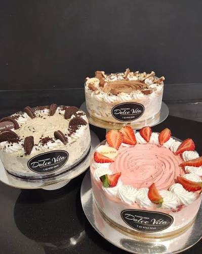 Three cakes topped with cream, biscuits, chocolate and strawberries, each with a Dolce Vita label